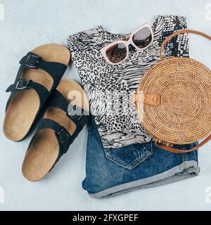 Flat lay avec vêtements et accessoires été pour femme. T-shirt à imprimé animal, short en denim bleu, sac en rotin biologique tendance, lunettes de soleil. Vacances, Banque D'Images