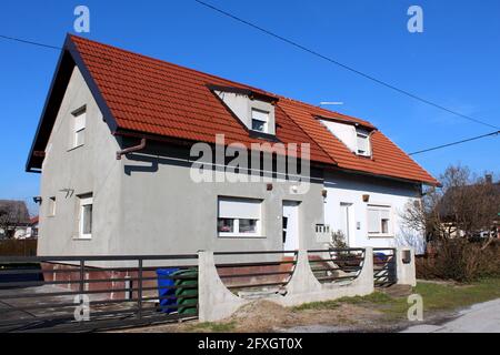 Petite maison familiale de banlieue partiellement rénovée avec deux entrées et plusieurs nouvelles fenêtres entourées de clôtures en béton et en métal Banque D'Images