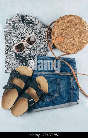 Flat lay avec vêtements et accessoires été pour femme. T-shirt à imprimé animal, short en denim bleu, sac en rotin biologique tendance, lunettes de soleil. Vacances, Banque D'Images