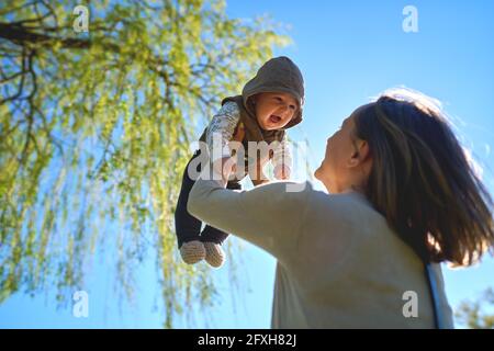 Silhouette de mère et de bébé au coucher du soleil. La mère jette l'enfant dans les airs. Banque D'Images