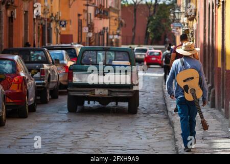 Musicien de rue marchant avec sa guitare dans les rues de la ville historique San Miguel de Allende à Guanajuato, Mexique. Banque D'Images