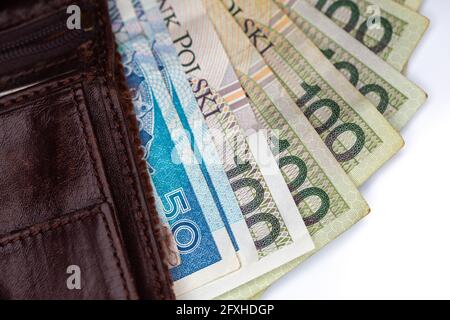 De nombreux billets polonais sortent d'un portefeuille en cuir marron. Photo prise sous lumière artificielle, douce, obisolée sur fond blanc Banque D'Images