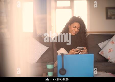 Une femme heureuse travaillant à la maison avec un smartphone et un ordinateur portable Banque D'Images