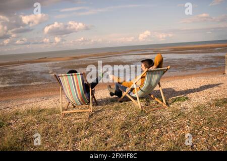 Couple toaster les verres à vin des chaises sur la plage ensoleillée d'hiver Banque D'Images