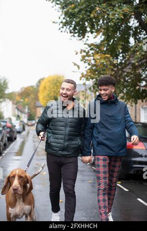 Heureux gay homme couple chien de marche sur la rue humide urbaine Banque D'Images