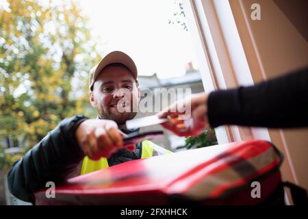 Homme payant le liveur pour la livraison de nourriture avec carte à puce à la porte d'entrée Banque D'Images