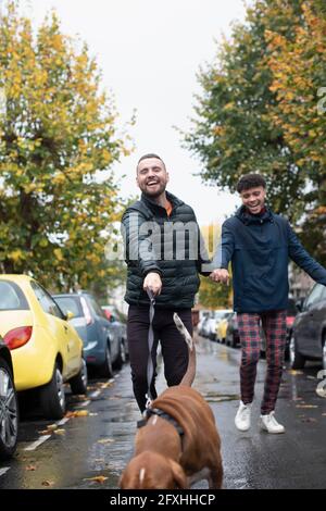 Heureux gay homme couple chien de marche sur la rue humide d'automne Banque D'Images