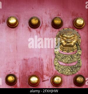 Ancienne porte en bois laquée rouge avec boutons épais et tête de lion décorée de deux décorations semi-circulaires dans la bouche en métal doré. Banque D'Images