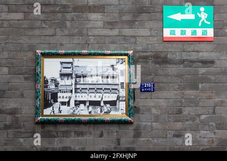 Image d'un bâtiment historique avec un cadre floral vert et jaune sur un mur en brique grise. Un petit signe multicolore avec une flèche. Banque D'Images