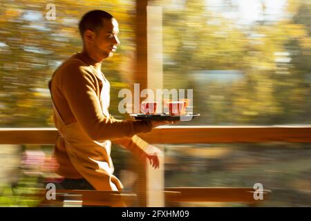 Un barista masculin porte un plateau de tasses de café le long de la fenêtre du café d'automne Banque D'Images