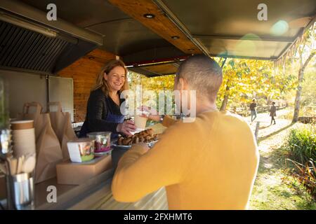 Sympathique propriétaire de chariot alimentaire servant du café au client dans le parc d'automne Banque D'Images