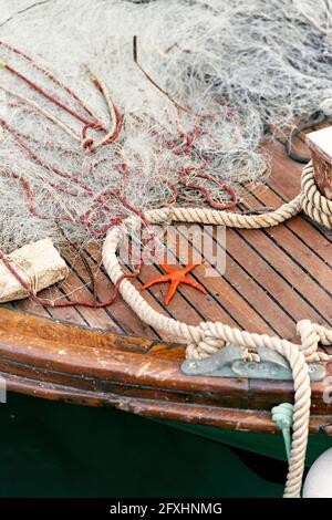 L'étoile de mer d'orange se trouve sur un pont en bois d'un bateau près d'une corde et d'un filet de pêche. Gros plan Banque D'Images