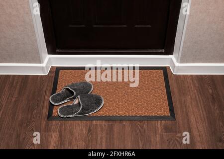 Vide le tapis de porte avant la porte sombre dans le hall. Chaussons à la maison sur le tapis. Vue de dessus du tapis sur le parquet. Une maquette pour votre conception Banque D'Images