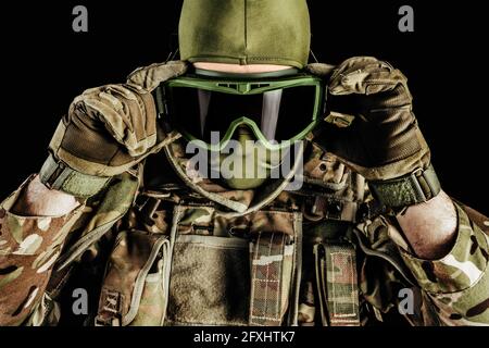 Photo d'un soldat dans des munitions blindées de niveau 3, gants tactiques mettant des lunettes tactiques sur fond noir. Banque D'Images