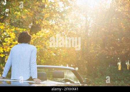 Jeune homme en décapotable se détendre en appréciant les arbres de parc d'automne ensoleillés Banque D'Images