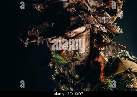 Photo d'un visage de chasseur masculin dans un chapeau de panama et un costume camouflé de forêt de guillie. Banque D'Images