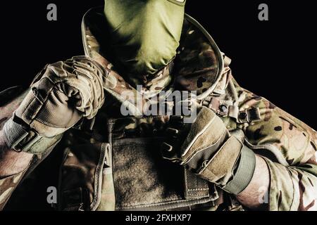 Photo d'un soldat dans des munitions de gilet blindé de niveau 3, gants tactiques mettant sur la protection du cou sur fond noir. Banque D'Images