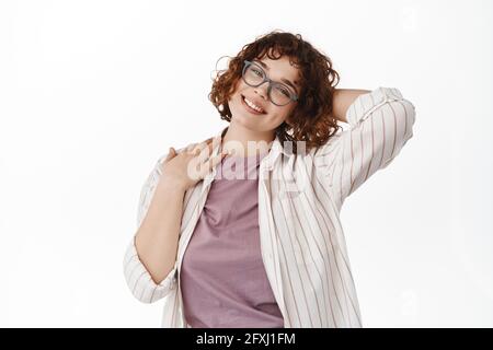 Portrait de la belle fille à poil dur en lunettes, se reposant et regardant heureux avec le sourire heureux, tenant la main derrière la tête détendue, appréciant des vacances Banque D'Images