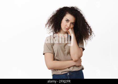 Image d'une femme brune réticente, se pencher à la main et regarder sans intérêt l'appareil photo, s'ennuyer, fatiguée de l'écoute, debout sur du blanc Banque D'Images