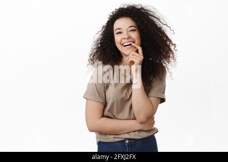 Belle jeune fille en forme de boutre sombre, souriant avec des dents blanches et regardant heureux l'appareil photo, ayez une idée intéressante, regardant pensive Banque D'Images