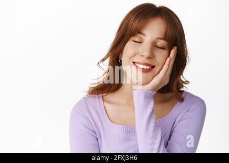 Belle femme souriante avec maquillage et lèvres rouges, rêvant, les yeux proches et se pencher sur la main romantique, souvenez-vous des souvenirs réconfortants Banque D'Images