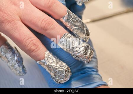 Faire du papier d'aluminium sur les ongles de la femme pendant la manucure. Ongles recouverts de papier d'aluminium pendant la procédure de retrait du gel lustrant. Banque D'Images