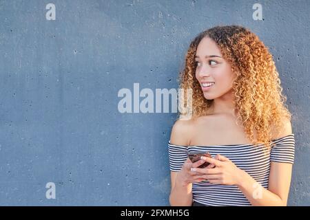 Jeune fille latina souriante tenant un smartphone à l'aide de la technologie d'application mobile à la maison. Bonne jeune fille hispanique textant, en vérifiant les applications de médias sociaux. Photo de haute qualité Banque D'Images