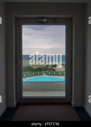 Vue panoramique maritime depuis la fenêtre panoramique du sol au plafond sur la mer méditerranée, le rivage rocheux et la piscine avec chaises longues à Ayia Napa Banque D'Images