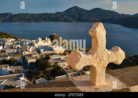 Croix chrétienne et village de Plaka sur l'île de Milos sur rouge Géranium fleurs au coucher du soleil en Grèce Banque D'Images