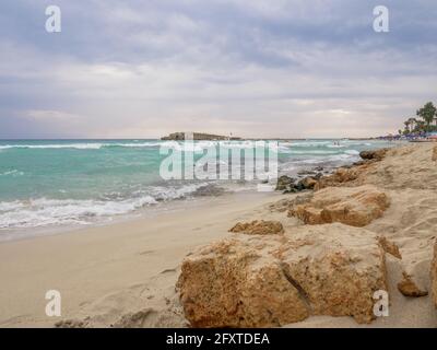 Vide pittoresque plage de Nissi avec l'eau cyan troublée, petite île rocheuse, et ciel sombre nuageux à Ayia Napa, Chypre. De merveilleuses vacances en mer. Banque D'Images