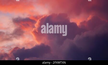 Paysage intense et vibrant avec des nuages illuminés dans différentes nuances de rose et de magenta contrastant avec au coucher du soleil. Banque D'Images