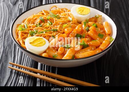 Rabokki ou combinaison de Ramyeon et Tteokbokki mélangé à l'oignon vert et à l'œuf dur. Gros plan de la nourriture épicée coréenne dans un bol sur la table. Horizontale Banque D'Images