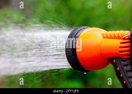 Aérosol d'eau orange. Arrosage du jardin vert. Pistolet à eau pour l'arrosage. Banque D'Images