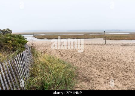 Vue sur le marais côtier lors d'une matinée d'automne brumeuse. Une clôture aux pieds de dunes de sable herbeuses est en premier plan. Banque D'Images