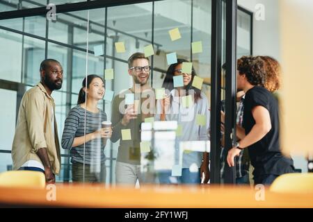 Une équipe amicale de collègues debout derrière le verre ensemble et travaillant Banque D'Images