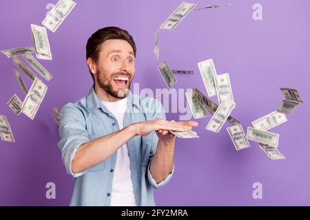 Photo de cool funky jeune homme porter Jean chemise sombre jeter de l'argent grande quantité isolé couleur violet arrière-plan Banque D'Images