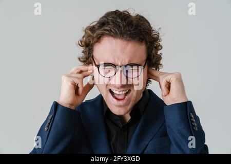 Stressé homme beau dans les lunettes criant et de brancher ses oreilles isolé sur fond blanc Banque D'Images