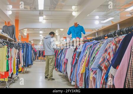 Ekaterinbourg, Russie - 31 mai 2020: Homme mature en masque choisissant des vêtements à la deuxième main magasin. Consommation consciente, un nouveau concept normal Banque D'Images