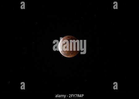 L'ombre de la terre tombe en partie sur une pleine lune alors qu'elle s'élève au-dessus d'un flanc de montagne pendant une éclipse lunaire totale vue d'Anilao dans la province de Batangas, au sud de Manille, Philippines. Banque D'Images