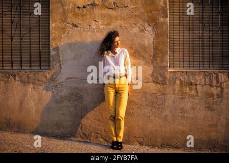 ANNÉES 1990 JEUNE FEMME TOURISTE PORTANT DES JEANS JAUNES DEBOUT ATTENTE DE REPOS CONTRE UN MUR DE STUC LAVÉ AU SOLEIL MAROC AFRIQUE - 161983 JAC003 HARS CONTRE LES FEMMES DE PLEINE LONGUEUR PERSONNES VILLAGE LUMIÈRE DU SOLEIL ÉTRANGÈRE AU REPOS TRISTESSE BRUNETTE TEMPS HORS AVENTURE STYLES VOYAGE ESCAPADE TOURISTE LAVÉ STUC A VACANCES HUMEUR ATLAS LONG CHEVEUX MODE ÉLÉGANT MOYEN-ADULTE VACANCES EN AFRIQUE DU NORD ETHNIE CAUCASIENNE MAROC À L'ANCIENNE Banque D'Images