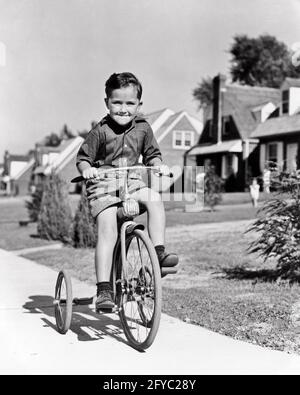 ANNÉES 1930 GARÇON DES ANNÉES 1940 À VÉLO TRICYCLE SUR UN TROTTOIR DE BANLIEUE SOURIANT UNE EXPRESSION DU VISAGE BIEN DÉTERMINÉE EN REGARDANT LA CAMÉRA - J5870 HAR001 HARS HOMMES BICYCLES TRANSPORT EXPRESSIONS B&W BIKES OEIL DE CONTACT LIBERTÉ BONHEUR TRICYCLE GAI AVENTURE LOISIR EXCITATION EXTÉRIEUR FIERTÉ SOURIRES JOYEUX FAIRE DU TRAFIC SINCÈRE DÉTERMINÉ SOLENNELLEMENT FOCALISÉ CROISSANCE INTENSE JUVÉNILES TRIKE NOIR ET BLANC PRUDENT DE L'ETHNICITÉ CAUCASIENNE SINCÈRE HAR001 INTENTION ANCIENNE Banque D'Images