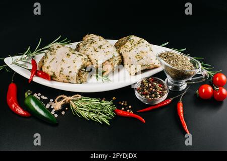 Viande pour le gril et le barbecue.cuisses de poulet crues sur fond sombre.cuisses de poulet crues en marinade blanche avec épices de romarin frais. Banque D'Images