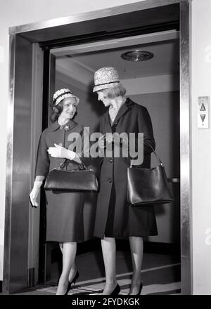 ANNÉES 1960 DEUX FEMMES QUI S'EN SONT À L'ASCENSEUR PARLENT EN PORTANT DES CHAPEAUX GANTS TRANSPORT DE SACS À MAIN - S14049 HAR001 HARS MANTEAUX COPIE PAS À PAS ESPACE AMITIÉ FEMMES PERSONNES FRÈRES ET SŒURS B&W D'ÂGE MOYEN BONHEUR LOISIRS STYLES ASCENSEUR LIEN FRÈRE CONNEXION BOURSES CONCEPTUELS MODE ÉLÉGANT ADULTE MOYEN ENSEMBLE NOIR ET BLANC RACE BLANCHE SAC À MAIN HAR001 DÉMODÉE Banque D'Images