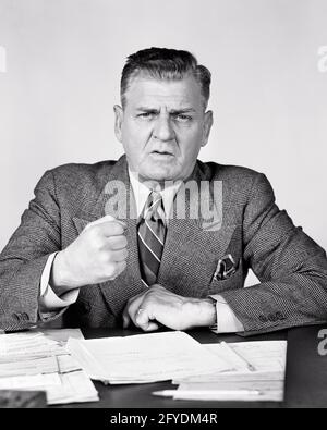 HOMMES D'AFFAIRES D'ÂGE MOYEN DES ANNÉES 1940 ASSIS AU BUREAU EXPRESSION DU VISAGE FRUSTRÉ ET EN COLÈRE SA MAIN UN POING SUR LE POINT DE REMETTRE LE BUREAU DANS RAGE - S7687 HAR001 HARS SOUCI STYLE DE VIE AGACÉ STUDIO TOURNÉ MOODY MANAGER ESPACE DE COPIE DEMI-LONGUEUR PERSONNES RÉFLÉCHIS HOMMES CADRES GESTURANT EXPRESSIONS TROUBLES B&W D'ÂGE MOYEN CONCERNE LA TRISTESSE HOMME D'ÂGE MOYEN CONTACT VISUEL COSTUME ET CRAVATE AFFLIGÉ EXCITATION GESTUELLE HUMEUR OCCUPATIONS PATRONS CONCEPTUEL EXIGEANT GLUM MÉCONTENTEMENT HOSTILITÉ SOLENNEL ENNUI ÉMOTION CONCENTRÉ ÉMOTIONNEL LES GESTIONNAIRES IRRITÉS INTENSE MISÉRABLE BLESSANT NOIR ET BLANC DE L'ORIGINE ETHNIQUE CAUCASIENNE Banque D'Images