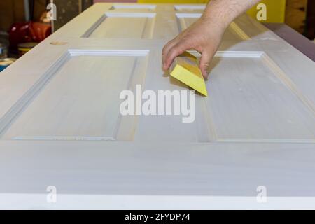 Menuisier dans le travail de l'ouvrier sablant la porte intérieure en bois après primaire avec bloc de ponçage Banque D'Images