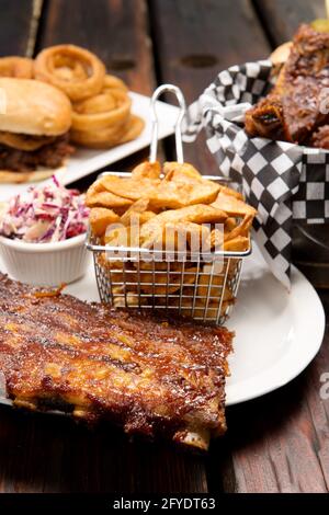 Barbecue restaurant sélection de nourriture. Côtes de porc grillées, côtes de bœuf, sandwich au porc tiré et sauce au bœuf avec frites maison. Banque D'Images