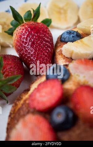 Gros plan de quelques fraises et bleuets tranchés sur deux crêpes sur un plat blanc et brillant Banque D'Images