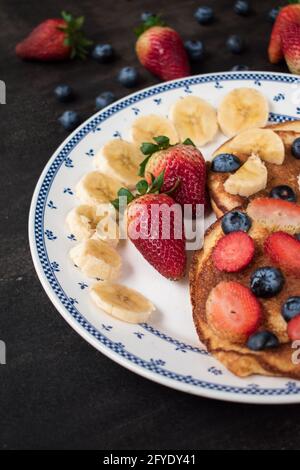 Quelques crêpes aux fraises douces, aux myrtilles et aux bananes tranchées sur une table noire avec un peu de fruits Banque D'Images