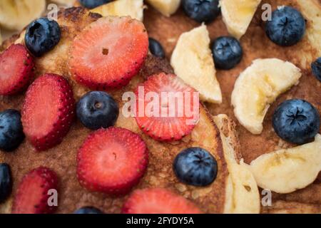 Gros plan de quelques fraises et bleuets tranchés sur deux crêpes sur un plat blanc et brillant Banque D'Images