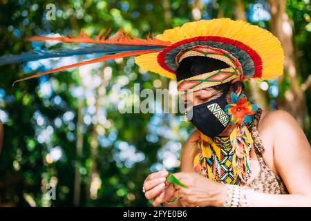 Indien de la tribu Pataxó avec une coiffe en plumes et un masque de protection. Femme indigène du Brésil faisant de l'artisanat Banque D'Images